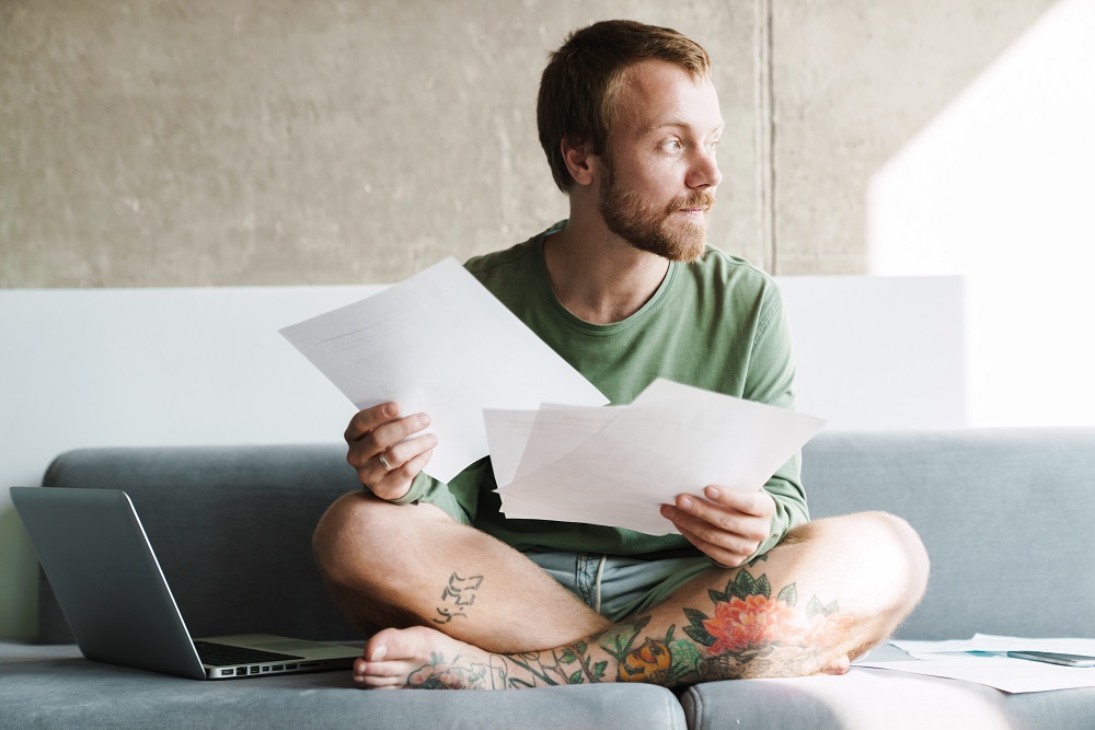 Photo of man working with laptop and papers while sitting on sofa
